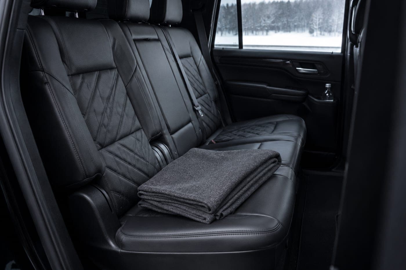 The second-row seats of a large black SUV, with a folded blanket
