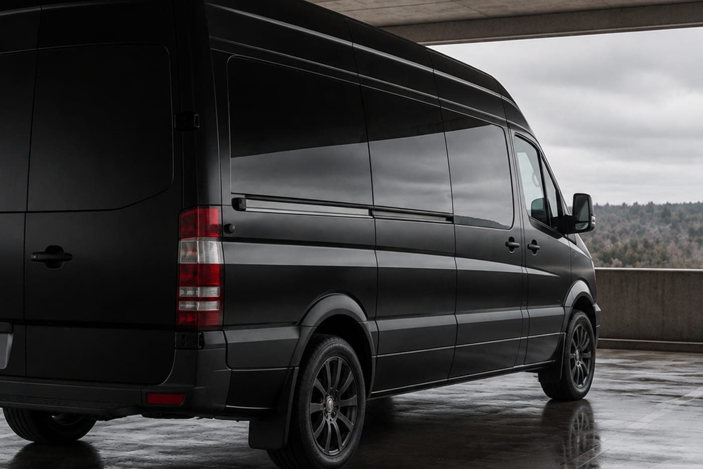 A black high-roof passenger van in a covered structure, seen from the rear